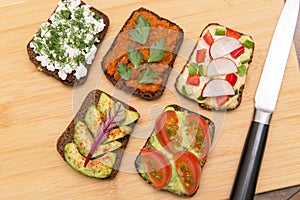 Various vegan, vegetarian healthy toasts on wooden board on kitchen with different vegetables, top view