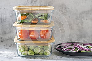 Various vegetables in glass containers: carrots, spinach, tomatoes, Brussels sprouts. Vegan food and snacks in containers, gray