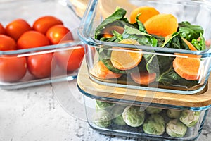 Various vegetables in glass containers: carrots, spinach, tomatoes, Brussels sprouts. Vegan food and snacks in containers, gray