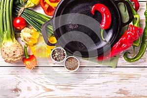 Various vegetables ingredients on wooden table around frying pan