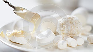 Various white candies, marshmallows and a spoon with peanut butter on a light