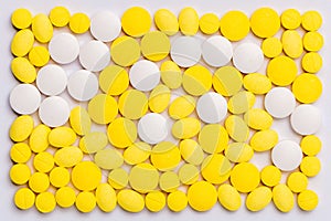 Various white and yellow medicine tablets spread as the background, medication treatment concept.