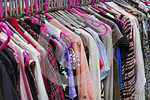 Various women clothing on mostly pink coat hangers inside charity second hand thrift shop photo