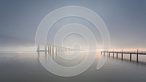 Long bridge over tagus river in Lisbon at sunrise with fog.