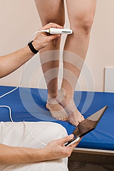 Vascular surgeon examines veins and arteries of legs of woman in medical clinic. Legs ultrasound examination scan using