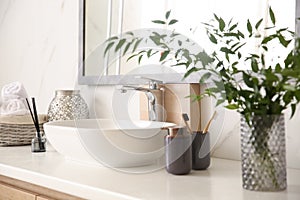 Vase with beautiful branches and toiletries near vessel sink in bathroom. Interior design