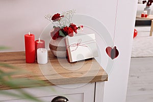 Vase with beautiful flowers, gift box and candles on wooden table indoors. Happy Valentine`s Day