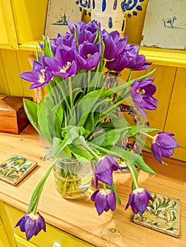 Vase of beautiful flowers. Purple tulips on yellow dresser.