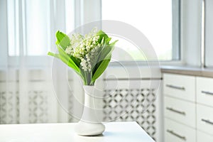 Vase with beautiful lily of the valley bouquet on table in room