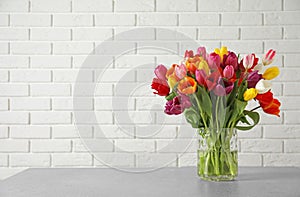 Vase with beautiful spring tulip flowers on table near brick wall.