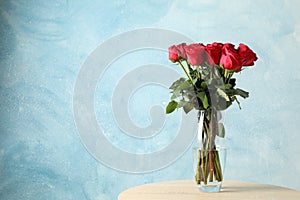 Vase with bouquet of red roses on table, space for text