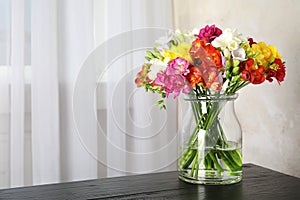 Vase with bouquet of spring freesia flowers on table in room