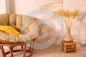 Vase with decorative dried plants and painting near papasan chair in stylish room interior