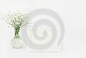 Vase with gypsophila flowers and a white photo frame on the table.