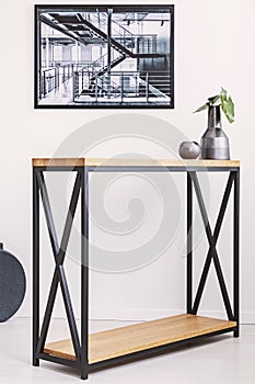 Vase with leaf and candle standing on stylish modern table with metal legs. Industrial poster on the wall