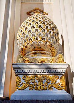 A vase made of plaster in the form of an egg with gilded segments standing on the facade of the building.