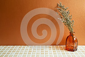 Vase of misty blue dry flowers on beige ceramic mosaic tile table. Orange background