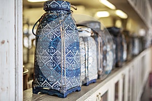 Vase in Oriental style with intricate ornament stands on a light wooden vintage shelf, in a row of many vintage vases, blurred