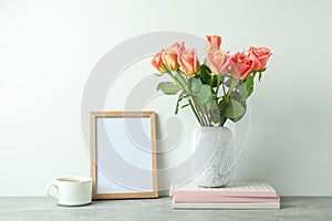 Vase with pink roses, copybooks, empty frame, cup of coffee on grey table