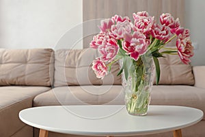 Vase of pink tulips on coffee table with blurred background of beige modern cozy light living room. Copy space