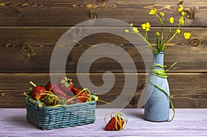 Vase with wildflowers. A basket of strawberries. One strawberry is on the table. Summer time