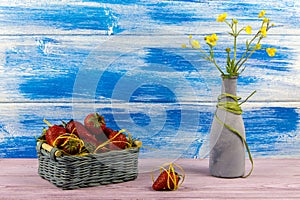 Vase with wildflowers. A basket of strawberries. One strawberry is on the table. Summer time