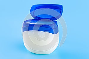 Vaseline or petroleum jelly in a clear jar on blue background with copy space for text. Skin care ointment