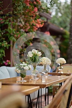 Vases with bouquets of white flowers on the table, bushes with flowers in the background