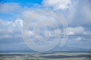 Vast, abstract landscape with hills in soft grey-green tones and a cloudy sky