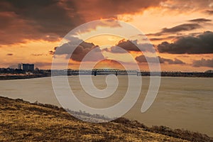 The vast flowing waters of the Mississippi river with a bridge over the water with powerful red clouds in the sky at sunset