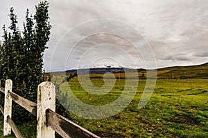 Vast green valley with a wooden fence mountains and a cloudy sky