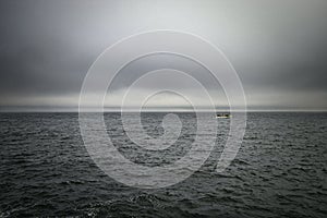 Vast grey ocean with asmall trawler fishing boat