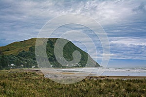 Vast ocean beach surrounded by rugged mountains. Heavy clouds and thick mist over riptide. Makorori beach, Gisborne