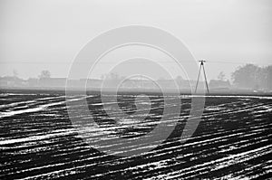 a vast, ploughed field with distinct furrows under an overcast sky, offering a view of a serene yet somber rural landscape Poland