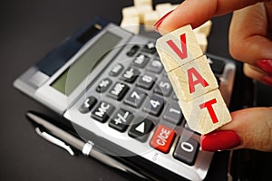 VAT calculation concept with woman hand holding vat word on wooden cubes above calculator keyboard on dark background