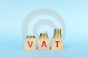 VAT letters on wooden blocks in blue background increasing stack of coins. Increase on value added tax