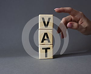 VAT - Value Added Tax symbol. Wooden cubes with word VAT. Businessman hand. Beautiful grey background. Business and Value Added