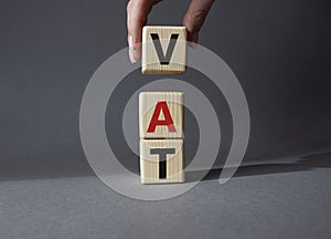 VAT - Value Added Tax symbol. Wooden cubes with word VAT. Businessman hand. Beautiful grey background. Business and Value Added