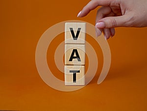 VAT - Value Added Tax symbol. Wooden cubes with word VAT. Businessman hand. Beautiful orange background. Business and Value Added