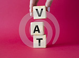 VAT - Value Added Tax symbol. Wooden cubes with word VAT. Businessman hand. Beautiful red background. Business and Value Added Tax