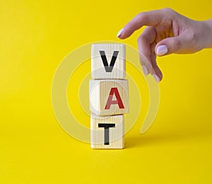 VAT - Value Added Tax symbol. Wooden cubes with word VAT. Businessman hand. Beautiful yellow background. Business and Value Added