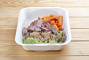 Veal sous vide with juicy carrots. Healthy diet. Takeaway food. Eco packaging. On a wooden background