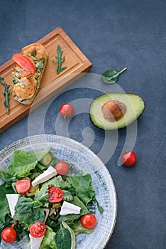 Vediterranean vegetable salad of fresh tomato, olives, capers, onion, spinach, lettuce and sesame on plate. Grillled shrimp