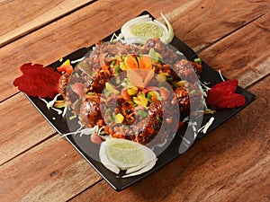 Veg Manchurian, Popular indo-chinese food made of cauliflower florets and other vegetable, served in a black plate over a rustic