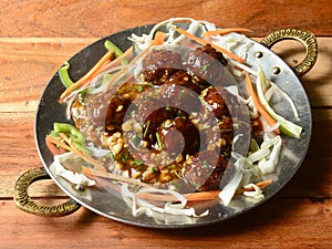 Veg Manchurian, Popular indo-chinese food made of cauliflower florets and other vegetable, served over a rustic wooden table.