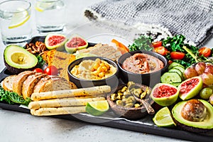 Vegan appetizer platter. Hummus, tofu, vegetables, fruits and bread on black tray, copy space