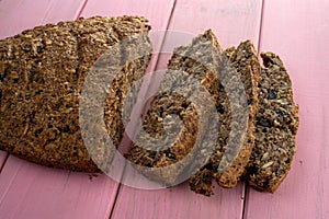 Vegan bread made from bran, flax, dried fruit, seeds, nuts, and other ingredients on a on pink wood texture
