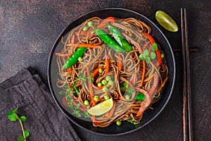 Vegan buckwheat soba noodles with vegetables in black plate on dark background, top view