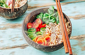 Vegan Buddha bowl. Healthy meal quinoa, tomato, cucumber, carrot, radish, corn salad in coconut bowls on blue rustic
