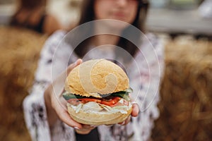 Vegan burger closeup in boho girl hands. Stylish hipster girl in sunglasses eating delicious vegan burger at street food festival